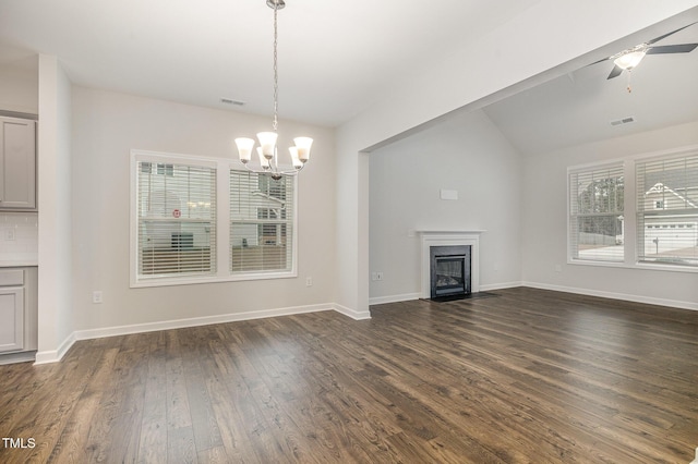 unfurnished living room with vaulted ceiling, a wealth of natural light, dark wood-type flooring, and ceiling fan with notable chandelier