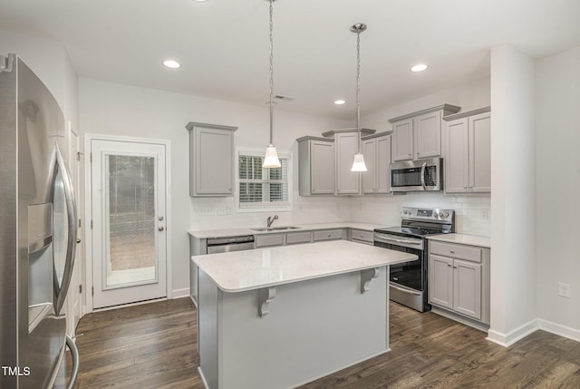 kitchen with sink, dark wood-type flooring, hanging light fixtures, a kitchen island, and appliances with stainless steel finishes