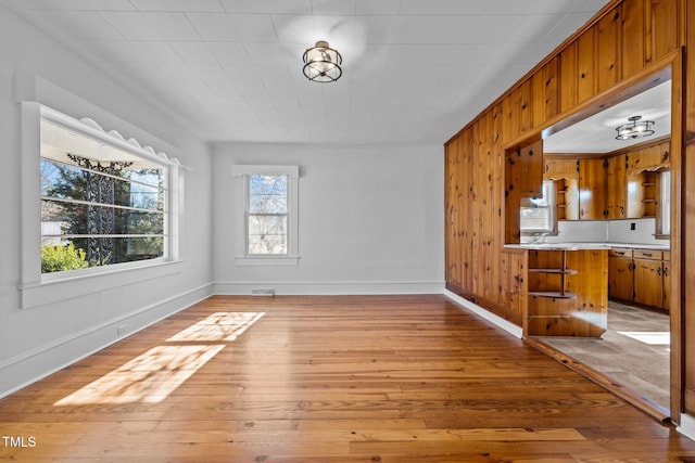 unfurnished dining area featuring wooden walls, plenty of natural light, and light wood-type flooring