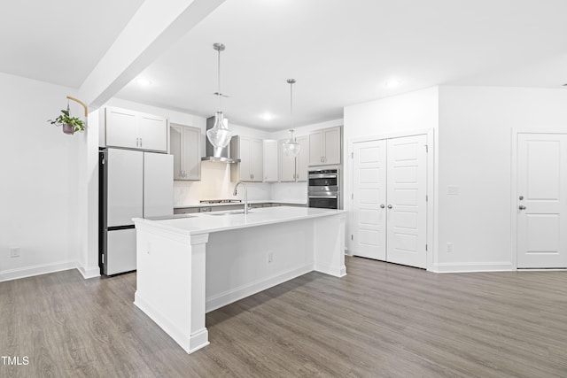 kitchen featuring stainless steel double oven, dark wood-type flooring, decorative light fixtures, white fridge, and an island with sink