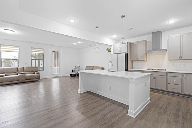 kitchen featuring wall chimney exhaust hood, gray cabinetry, stainless steel gas cooktop, a kitchen island with sink, and white refrigerator