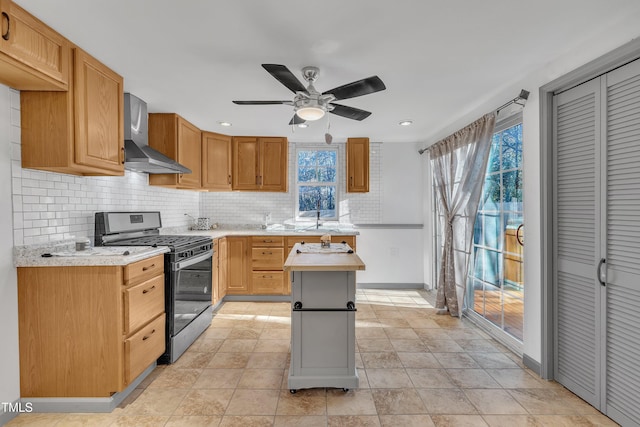 kitchen featuring backsplash, wall chimney exhaust hood, gas stove, ceiling fan, and a kitchen island