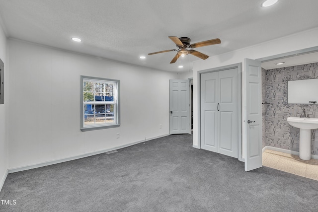 unfurnished bedroom featuring ensuite bathroom, a textured ceiling, ceiling fan, sink, and dark colored carpet