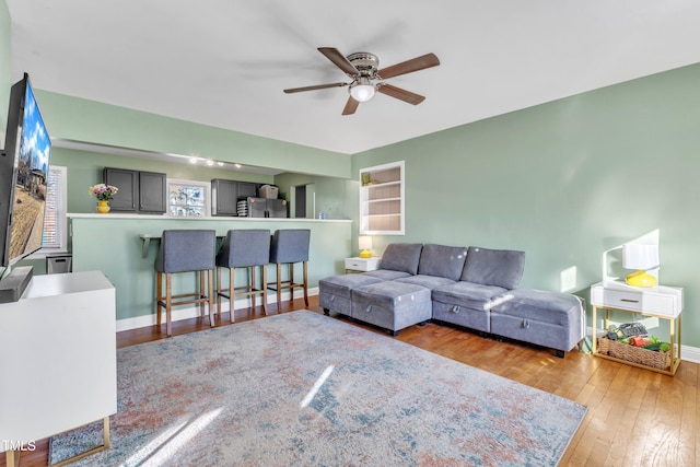 living room featuring built in shelves, light hardwood / wood-style floors, and ceiling fan