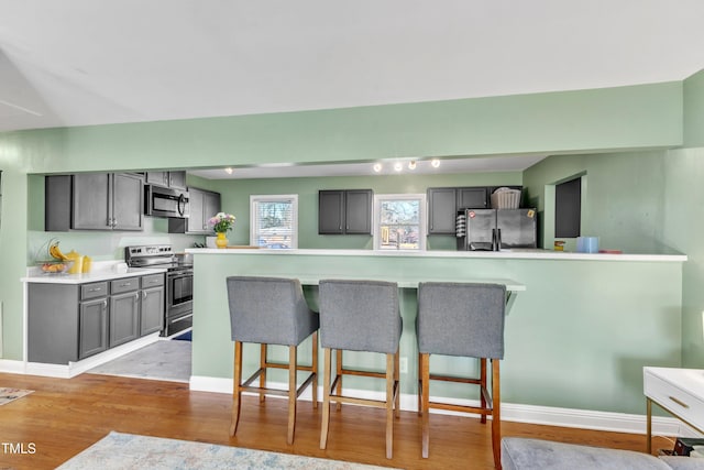 kitchen featuring gray cabinetry, light hardwood / wood-style floors, a kitchen bar, and stainless steel appliances