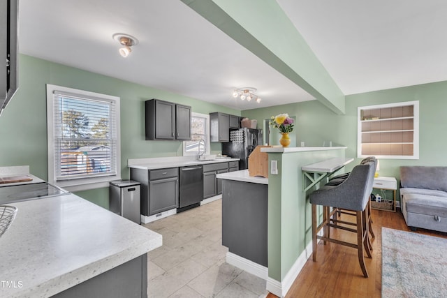 kitchen with black refrigerator, a kitchen breakfast bar, stainless steel dishwasher, gray cabinetry, and sink