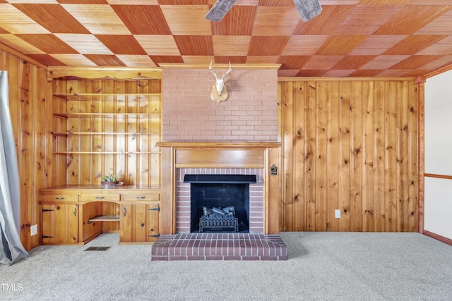 unfurnished living room featuring wooden walls, light colored carpet, wood ceiling, and a brick fireplace