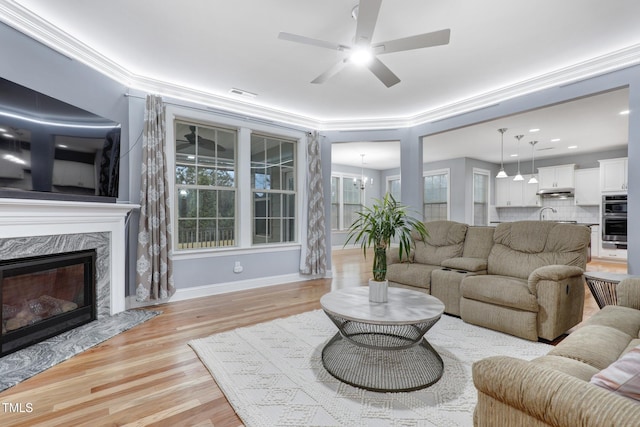 living area featuring a high end fireplace, visible vents, baseboards, ornamental molding, and light wood-type flooring