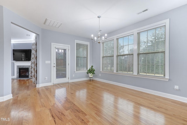 unfurnished dining area with light wood-type flooring, baseboards, an inviting chandelier, and a premium fireplace