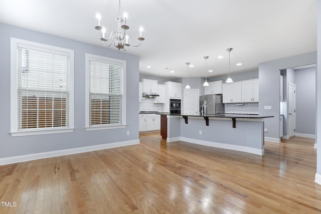 kitchen with a breakfast bar, dark countertops, decorative backsplash, stainless steel fridge, and under cabinet range hood