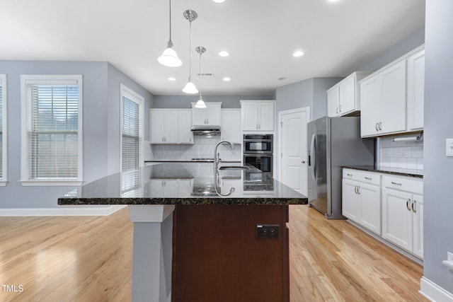 kitchen featuring stainless steel appliances, a sink, white cabinetry, hanging light fixtures, and light wood finished floors