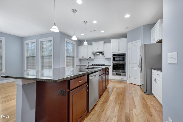 kitchen with stainless steel appliances, visible vents, backsplash, light wood-style flooring, and a sink