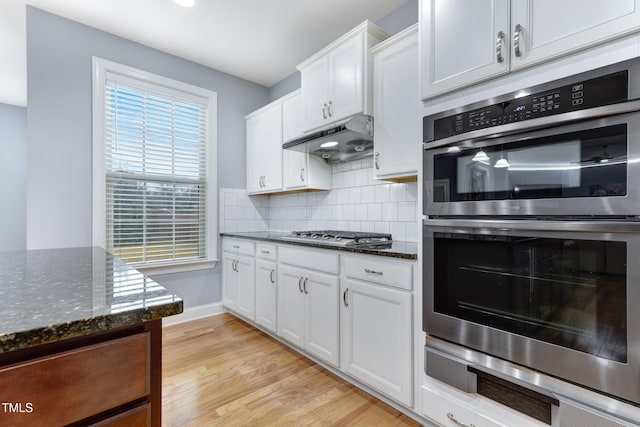 kitchen featuring under cabinet range hood, white cabinets, light wood-style floors, appliances with stainless steel finishes, and decorative backsplash