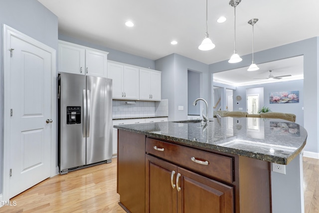 kitchen featuring a sink, backsplash, light wood finished floors, dark stone countertops, and stainless steel fridge