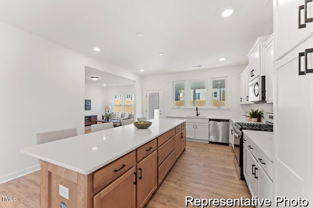 kitchen featuring light wood-type flooring, stainless steel appliances, sink, a center island, and white cabinetry