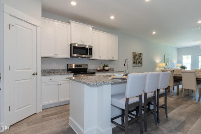 kitchen with a kitchen island with sink, white cabinets, stainless steel appliances, and wood-type flooring