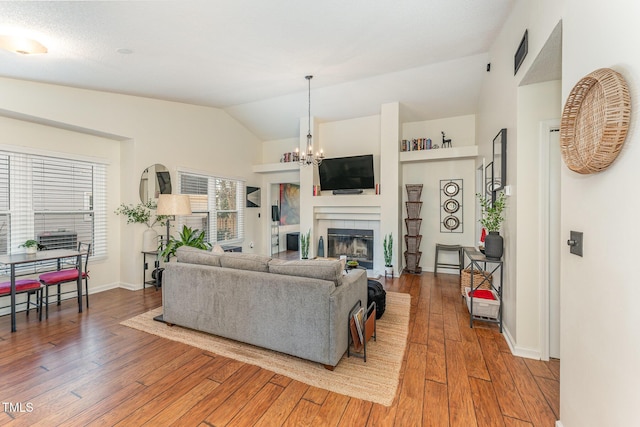 living room featuring a fireplace, wood-type flooring, lofted ceiling, and a notable chandelier