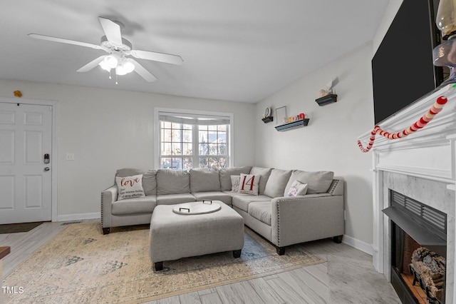 living room with a high end fireplace, ceiling fan, baseboards, and wood finished floors