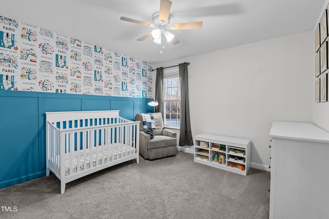 carpeted bedroom featuring wainscoting, ceiling fan, and a crib