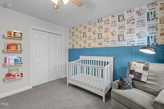 carpeted bedroom with a crib, a closet, wainscoting, and a ceiling fan