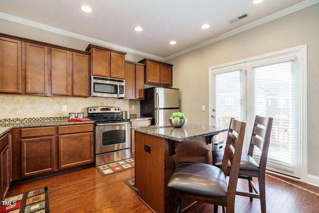 kitchen featuring stainless steel appliances, a kitchen bar, light stone countertops, a kitchen island, and crown molding