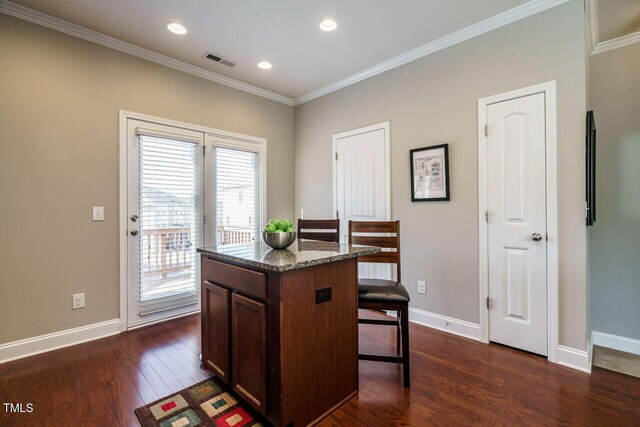 interior space with a center island, stone counters, a kitchen breakfast bar, ornamental molding, and dark hardwood / wood-style floors