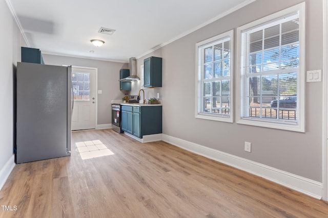 kitchen featuring appliances with stainless steel finishes, blue cabinets, wall chimney range hood, crown molding, and light hardwood / wood-style flooring