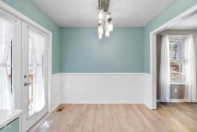 unfurnished dining area featuring french doors, light hardwood / wood-style floors, and a notable chandelier