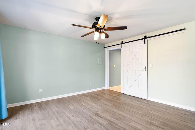 unfurnished bedroom with a barn door, ceiling fan, and hardwood / wood-style floors