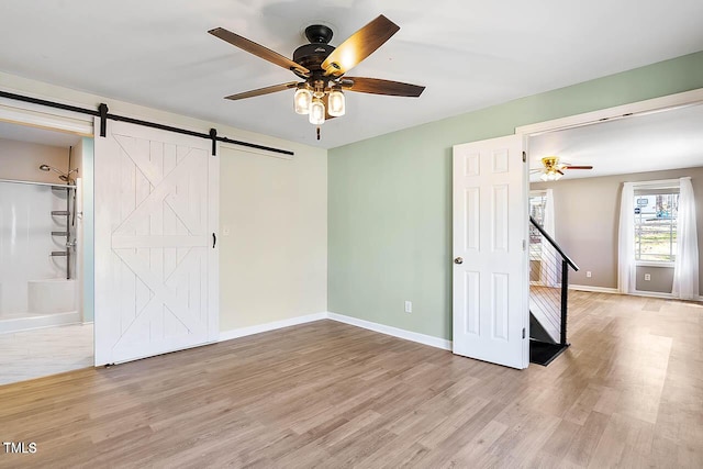 interior space with ceiling fan, a barn door, and light hardwood / wood-style floors