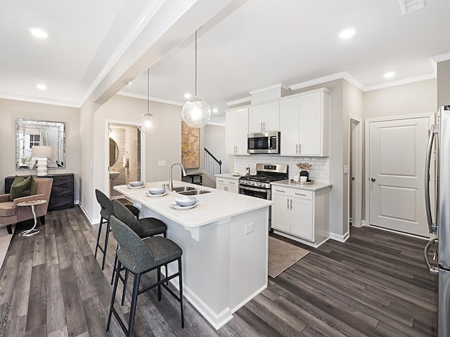 kitchen featuring white cabinetry, sink, hanging light fixtures, stainless steel appliances, and an island with sink