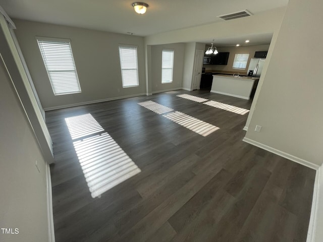 unfurnished living room with a healthy amount of sunlight, dark hardwood / wood-style floors, and a notable chandelier