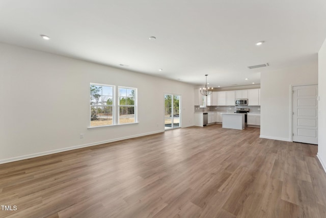 unfurnished living room with an inviting chandelier and light hardwood / wood-style floors