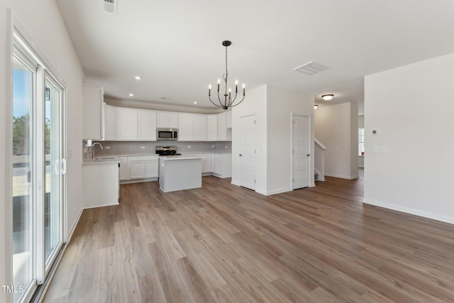 kitchen featuring appliances with stainless steel finishes, decorative light fixtures, white cabinets, backsplash, and light wood-type flooring