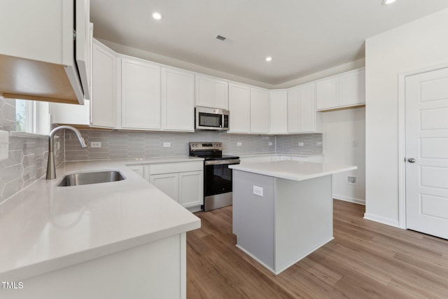 kitchen with sink, appliances with stainless steel finishes, white cabinets, a kitchen island, and light wood-type flooring