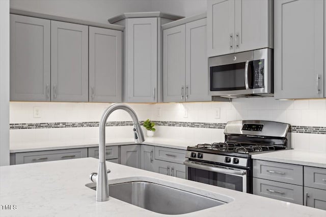 kitchen featuring gray cabinetry, sink, stainless steel appliances, and light stone countertops