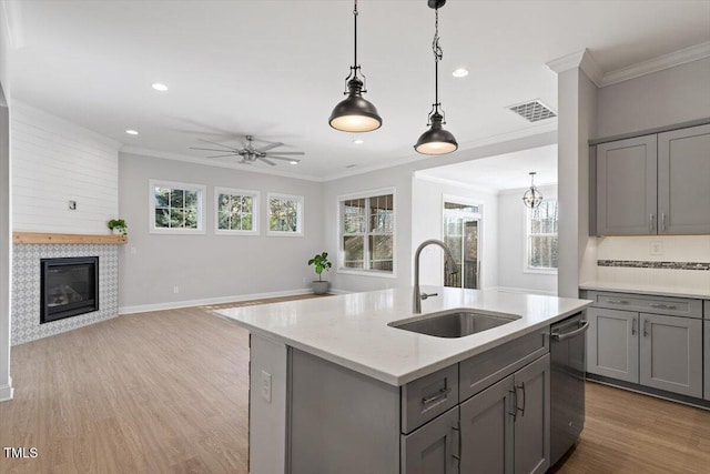 kitchen with an island with sink, sink, stainless steel dishwasher, and gray cabinetry