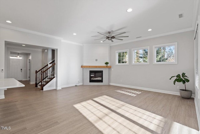 unfurnished living room with a tiled fireplace, ornamental molding, ceiling fan, and light wood-type flooring