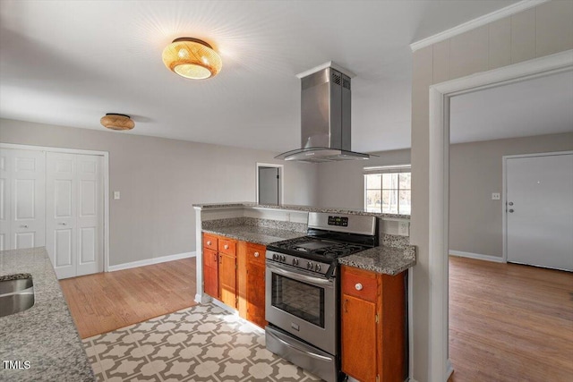 kitchen with sink, island range hood, light wood-type flooring, stainless steel range with gas stovetop, and stone counters