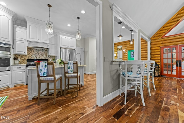 kitchen with log walls, light stone countertops, appliances with stainless steel finishes, and white cabinetry