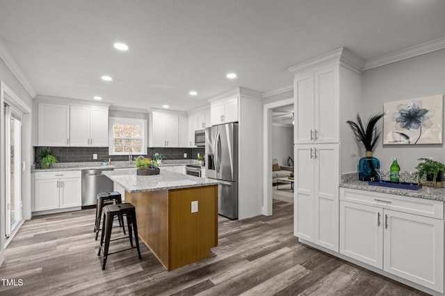 kitchen featuring white cabinetry, stainless steel appliances, decorative backsplash, light stone countertops, and a center island