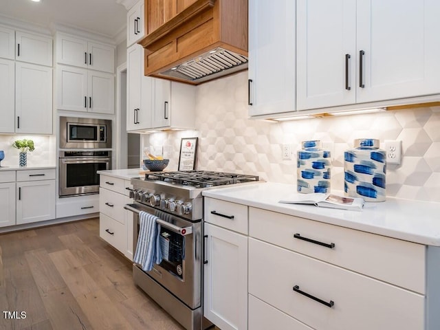 kitchen featuring white cabinets, custom exhaust hood, stainless steel appliances, tasteful backsplash, and light hardwood / wood-style floors