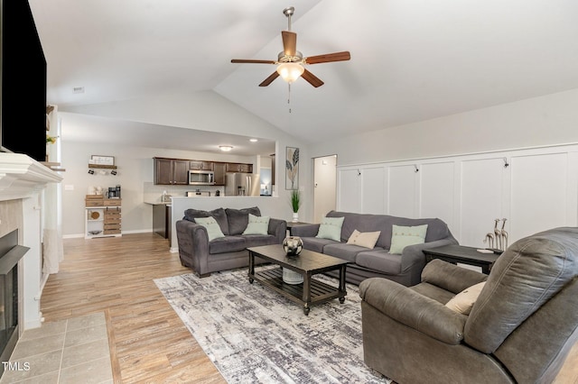 living room with light wood-type flooring, vaulted ceiling, ceiling fan, and a tile fireplace