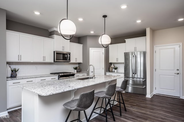 kitchen with stainless steel appliances, a kitchen island with sink, sink, pendant lighting, and white cabinets