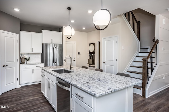 kitchen featuring appliances with stainless steel finishes, sink, decorative light fixtures, white cabinets, and an island with sink