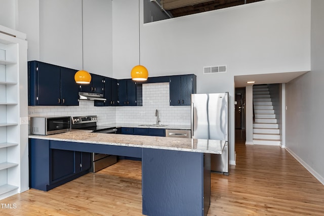 kitchen featuring a towering ceiling, blue cabinetry, a kitchen bar, kitchen peninsula, and stainless steel appliances