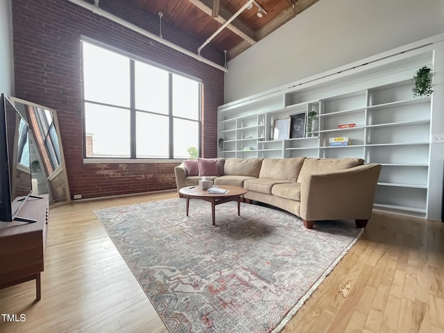 living room with beam ceiling, light wood-type flooring, wood ceiling, and brick wall