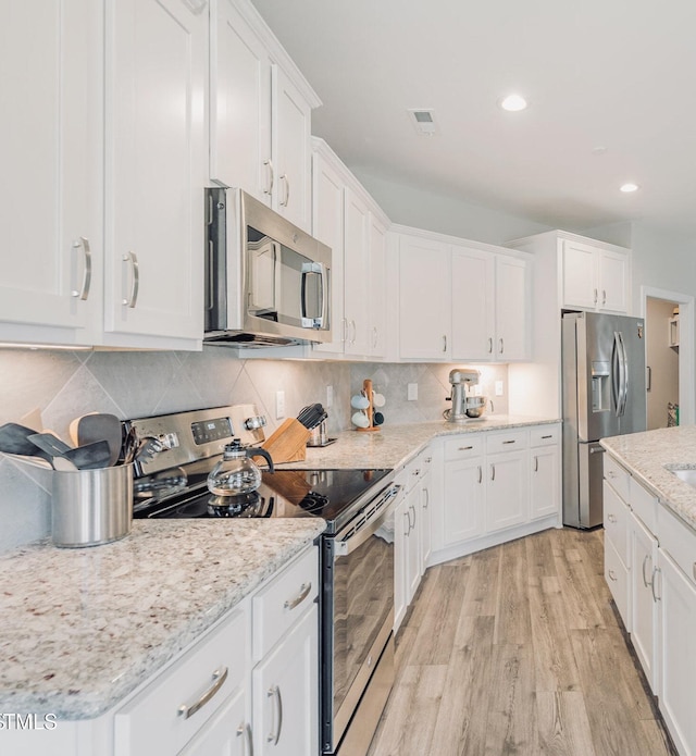 kitchen with white cabinets, decorative backsplash, stainless steel appliances, and light hardwood / wood-style floors