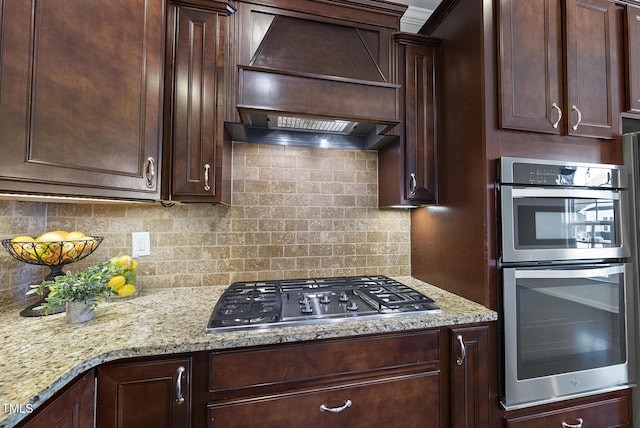 kitchen with light stone countertops, appliances with stainless steel finishes, custom range hood, and backsplash