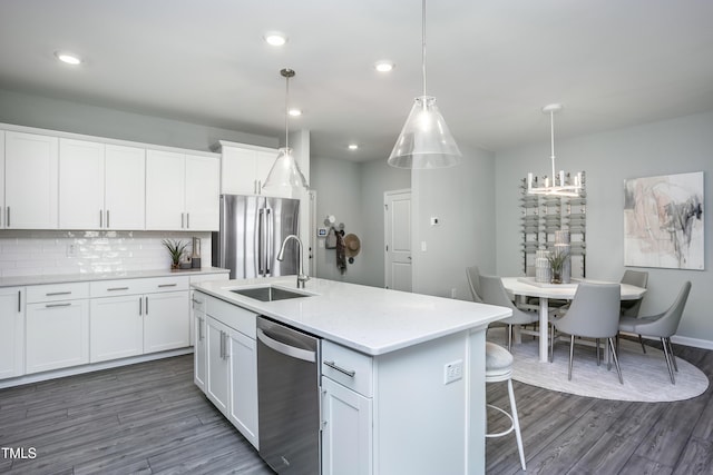 kitchen with appliances with stainless steel finishes, a kitchen island with sink, sink, pendant lighting, and white cabinetry